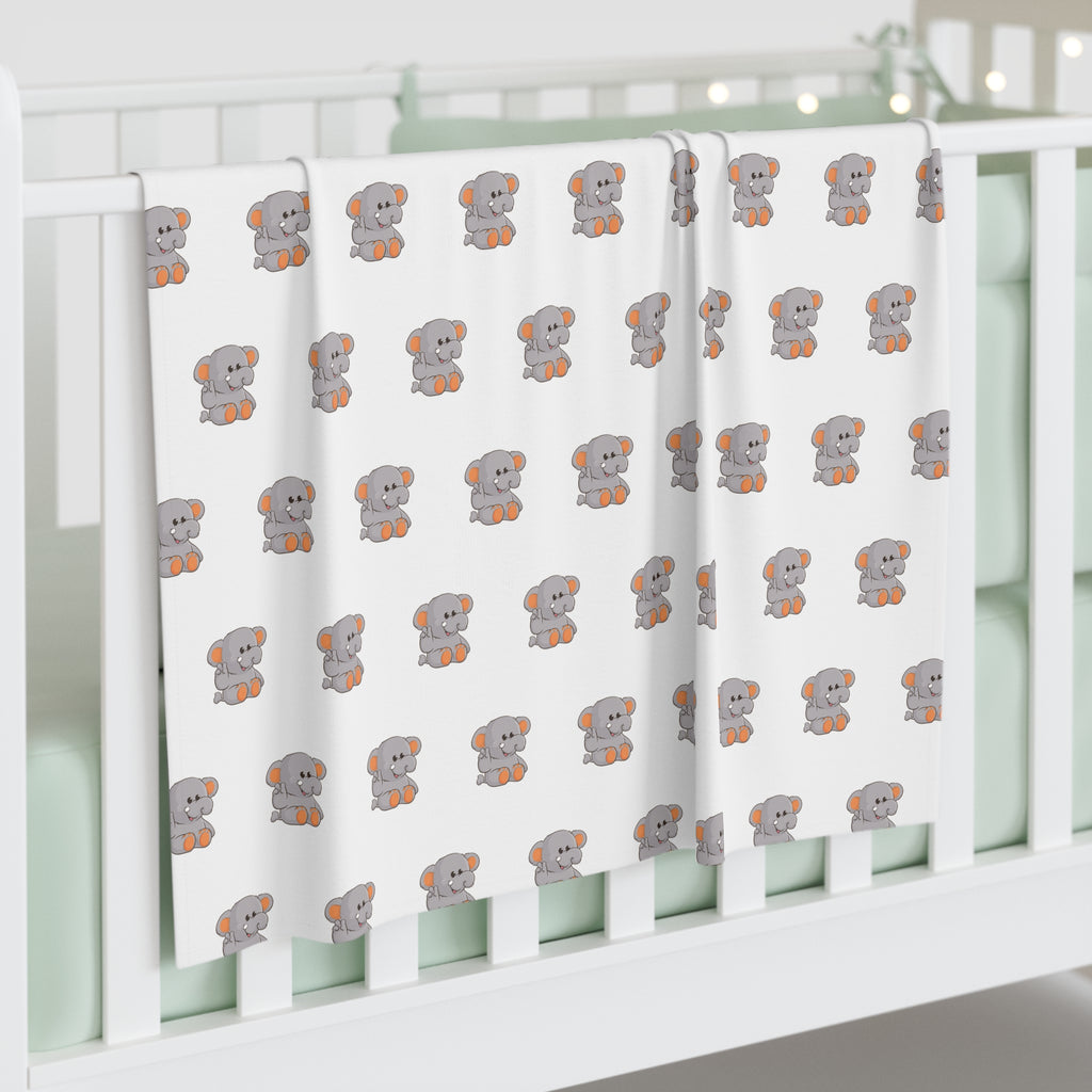 A white swaddle blanket with a repeating pattern of an elephant. The blanket is draped over the side of a baby crib.