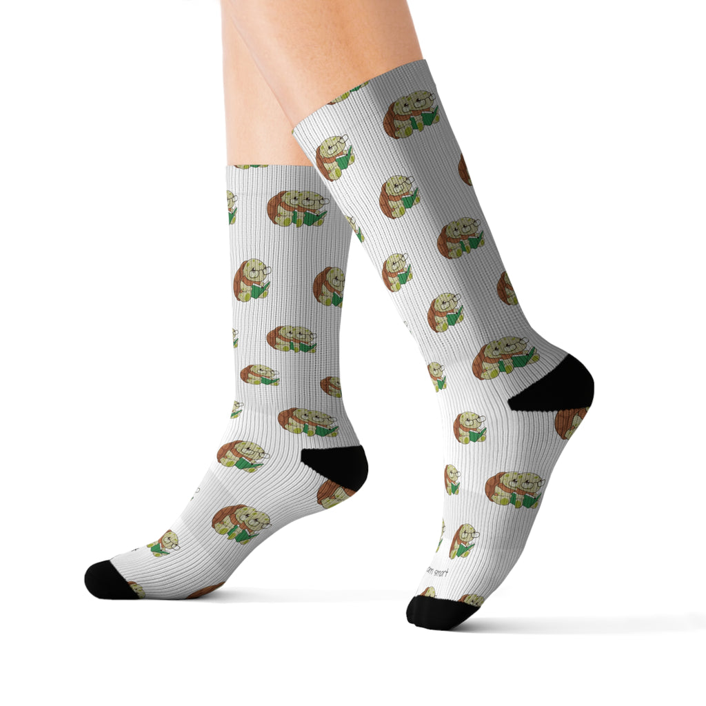 Feet wearing a pair of crew-length white socks with black toes and heels and a repeating pattern of a turtle.