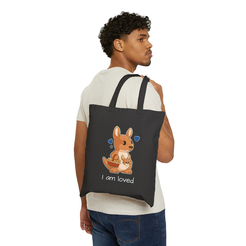 A man with a black tote bag over his shoulder, featuring a picture of a kangaroo that says I am loved.