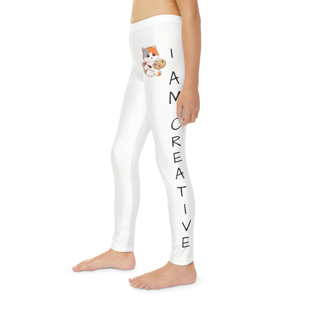 Left side-view of a child wearing white leggings with a picture of a cat on the front left waist and the phrase "I am creative" read top to bottom on the side of each leg.