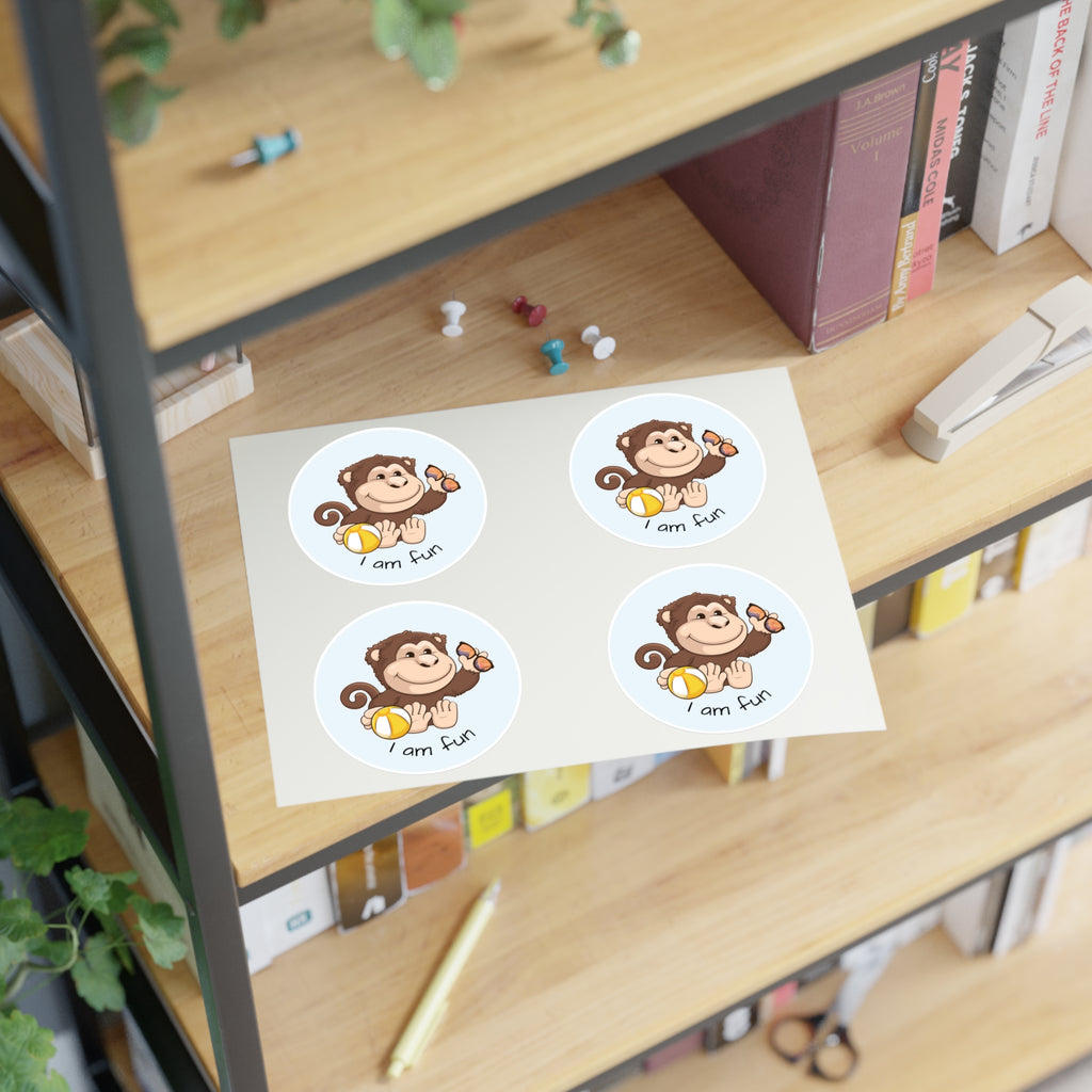 A sheet of 4 round stickers with a picture of a monkey that says I am fun. The sticker sheet sits on a shelf of a bookcase.
