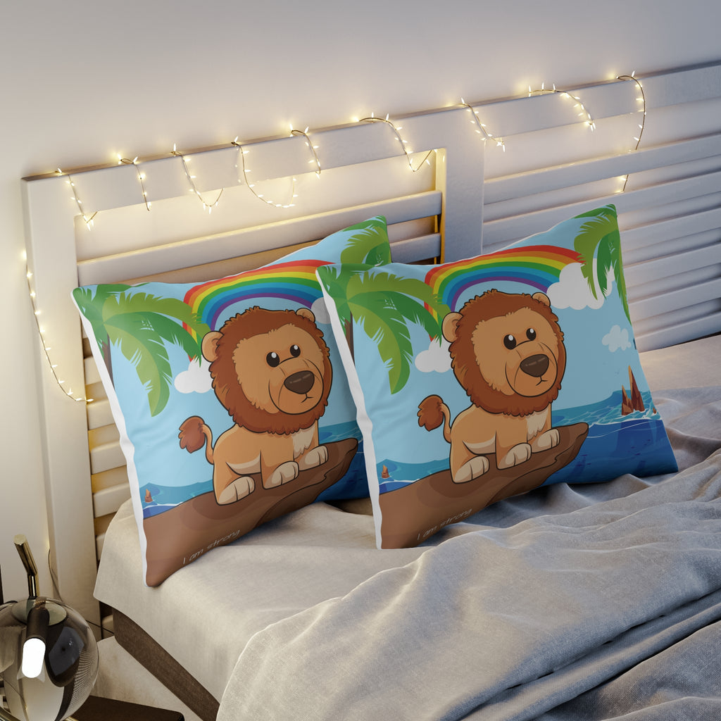 Two pillows sitting on a bed. The pillows have on pillowcases with a scene of a lion standing on a cliff over the ocean, a rainbow in the background, and the phrase "I am strong" along the bottom.