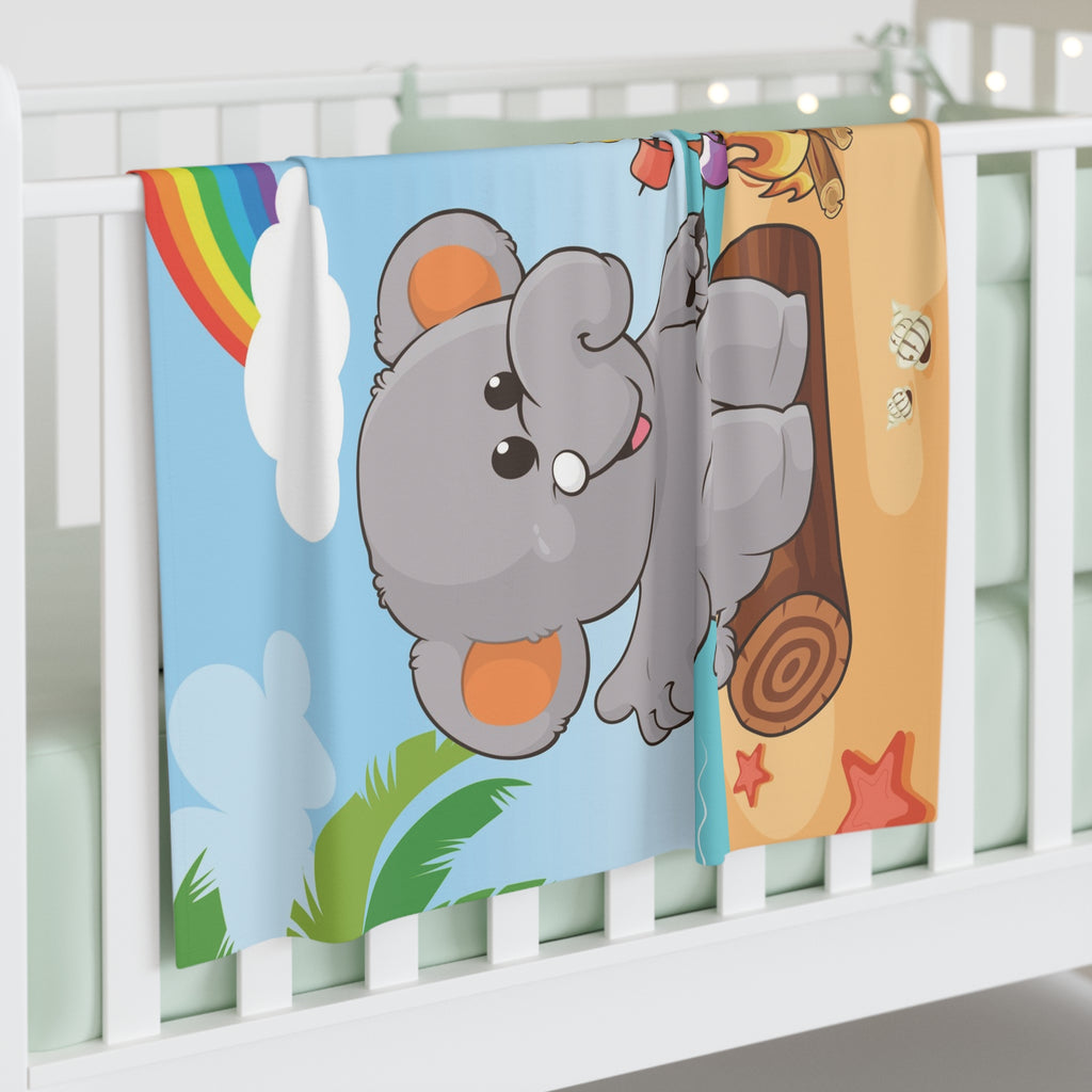 Full-color swaddle blanket with a scene of an elephant having a bonfire with a bird and fish on the beach, a rainbow in the background, and the phrase "I am calm" along the bottom. The blanket is draped over the side of a baby crib.