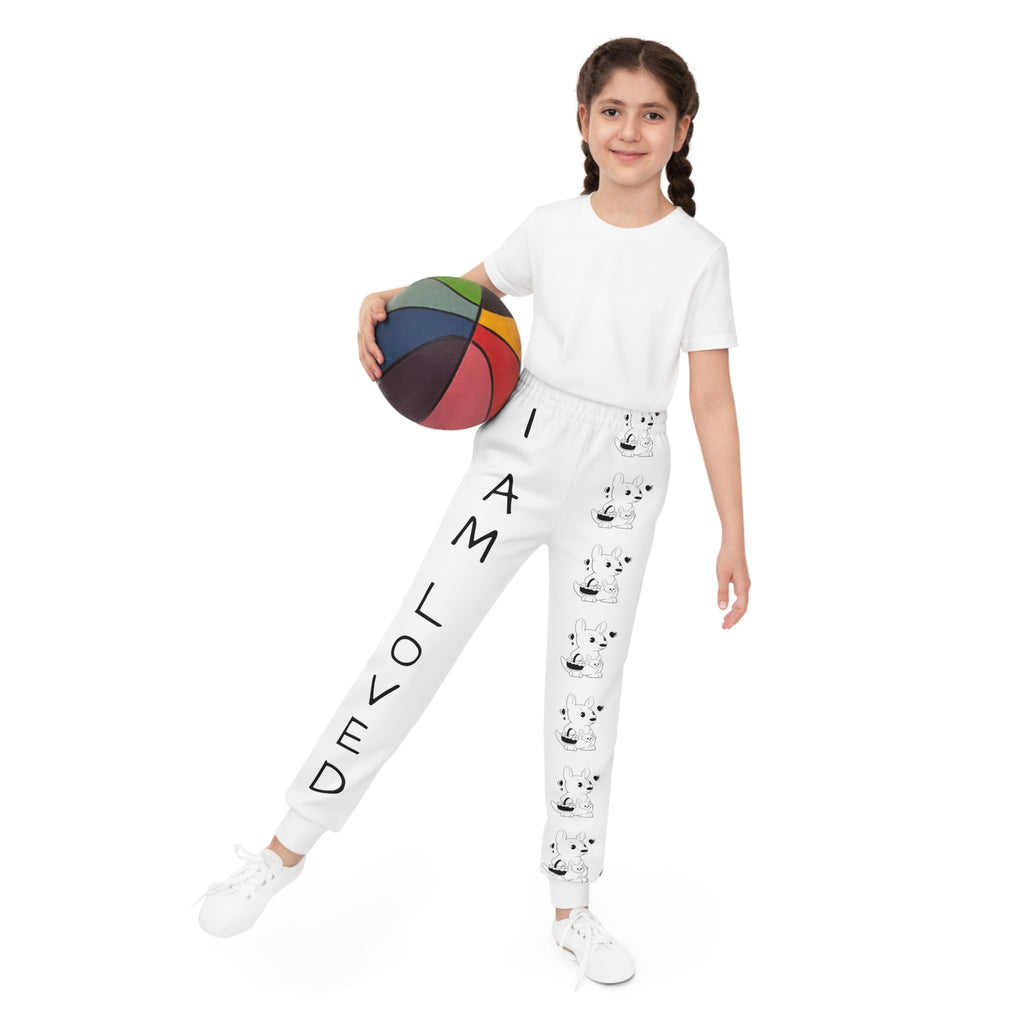 Front-view of a girl holding a basketball and wearing white sweatpants. The pants have a line of black and white kangaroos down the front left leg and the phrase "I am loved" down the front right leg.