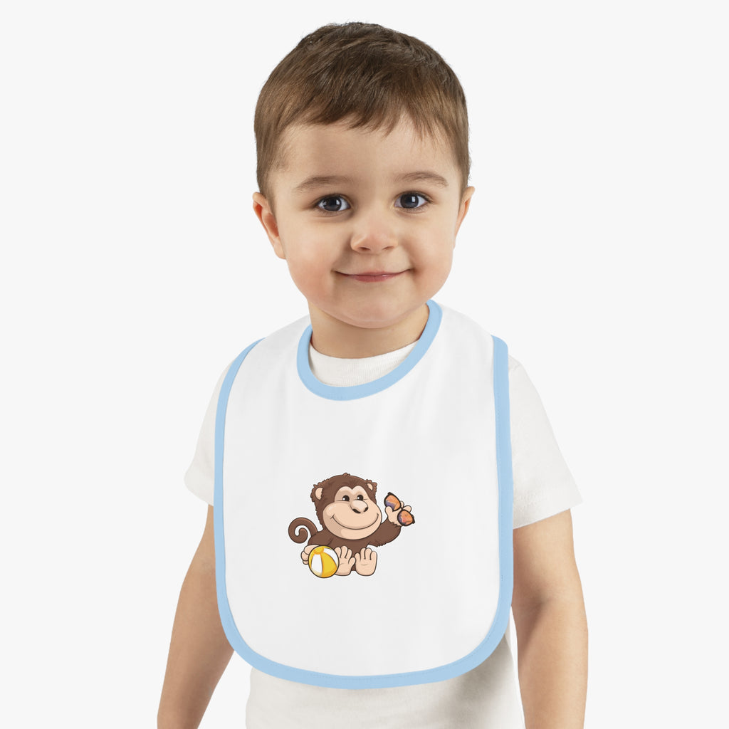 A little boy wearing a white baby bib with light blue trim and a small picture of a monkey.