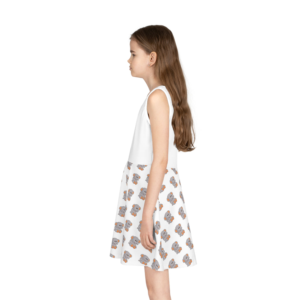Left side-view of a girl wearing a sleeveless white dress with a white top and a repeating pattern of an elephant on the skirt.