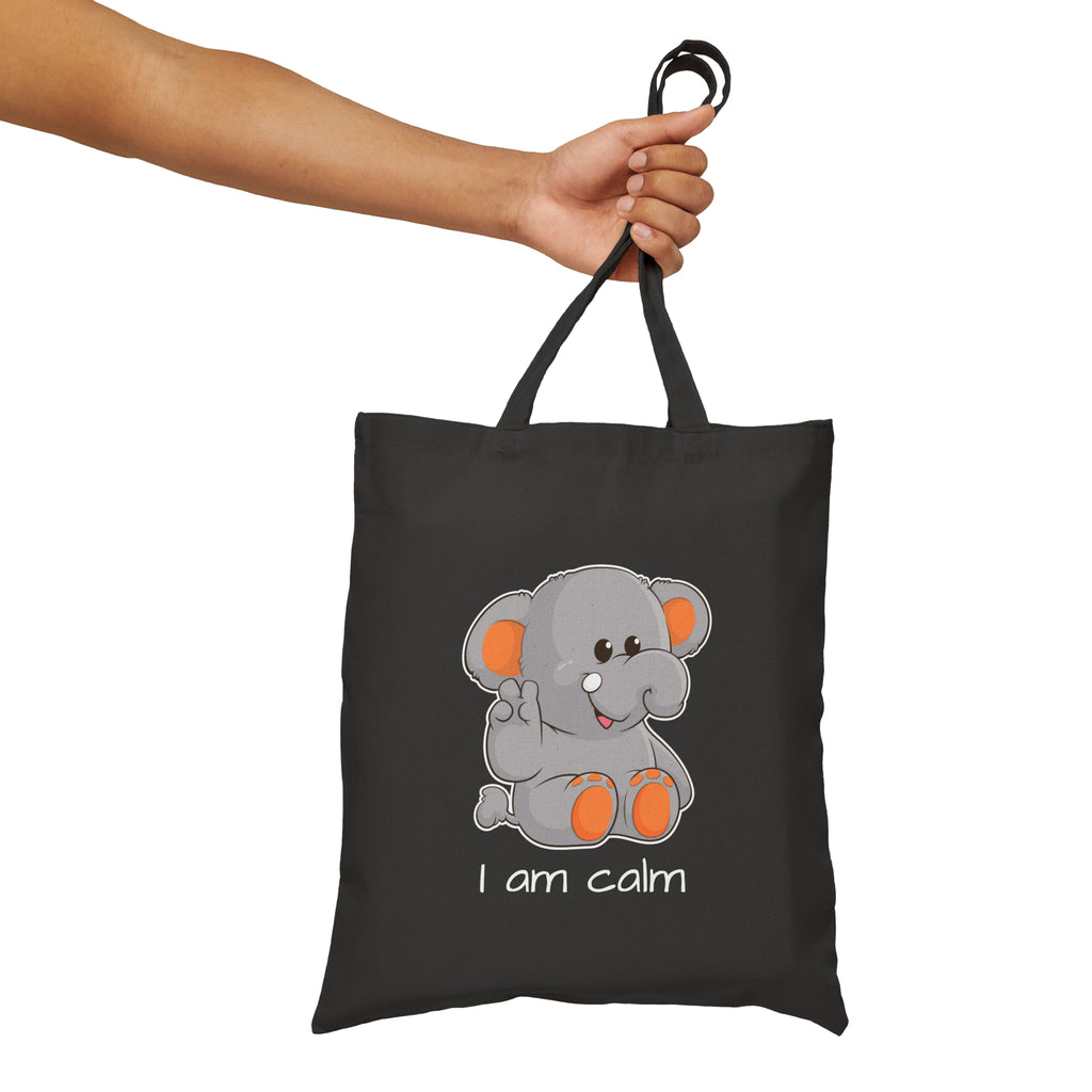 A hand holding a black tote bag with a picture of an elephant that says I am calm.