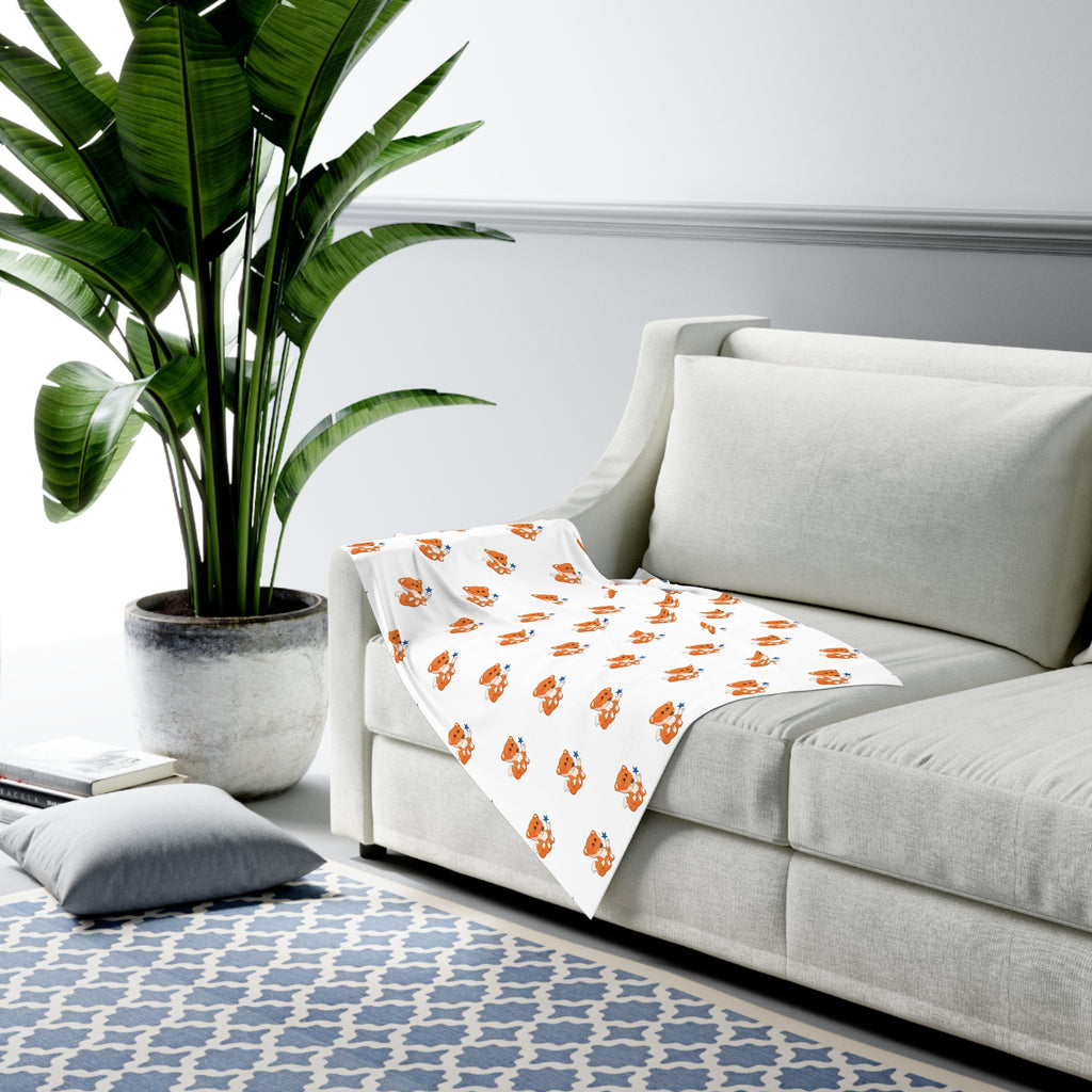 A white swaddle blanket with a repeating pattern of a fox. The blanket is draped over the armrest of a couch.