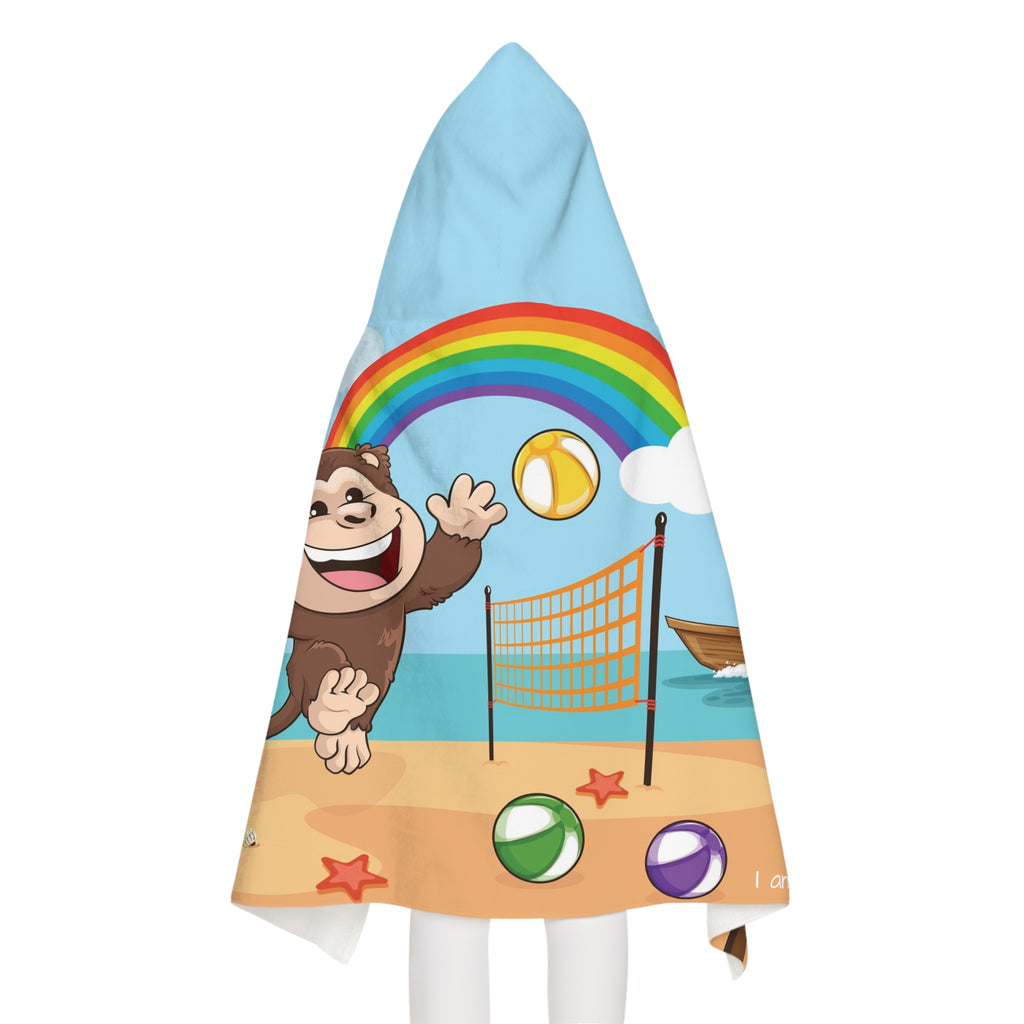 Back-view of a girl wearing a hooded towel. The towel has a scene of a monkey playing volleyball on the beach, a rainbow in the background, and the phrase "I am fun" along the bottom.