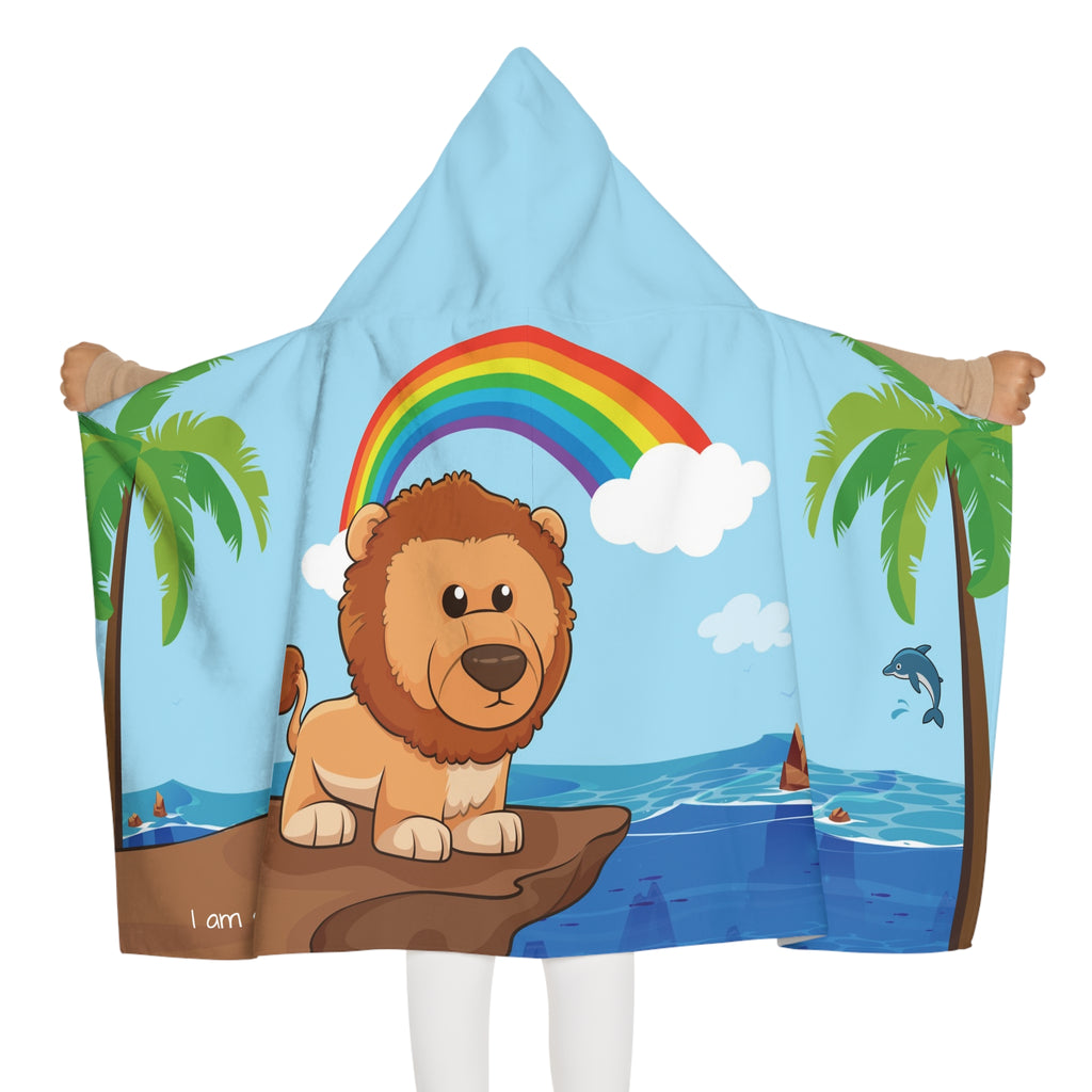 Back-view of a girl wearing a hooded towel and holding it open. The towel has a scene of a lion standing on a cliff over the ocean, a rainbow in the background, and the phrase "I am strong" along the bottom.