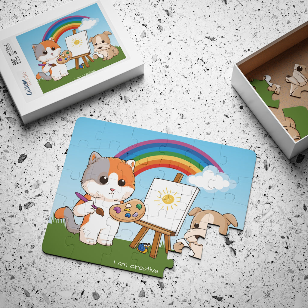 A 30 piece puzzle with a scene of a cat painting on a canvas next to a dog, a rainbow in the background, and the phrase "I am creative" along the bottom. The puzzle is mostly assembled next to its container box.