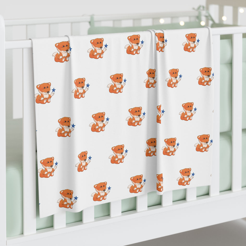 A white swaddle blanket with a repeating pattern of a fox. The blanket is draped over the side of a baby crib.