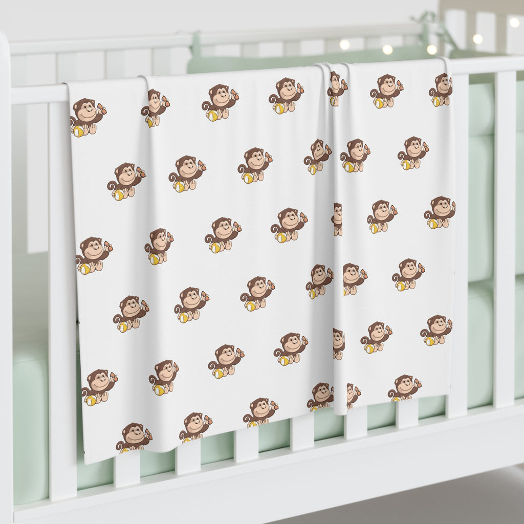 A white swaddle blanket with a repeating pattern of a monkey. The blanket is draped over the side of a baby crib.