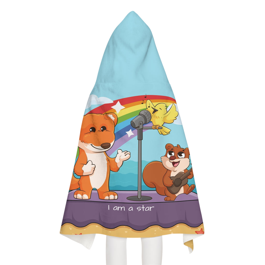 Back-view of a girl wearing a hooded towel. The towel has a scene of a fox singing with a bird and squirrel on a stage on the beach, a rainbow in the background, and the phrase "I am a star" along the bottom.