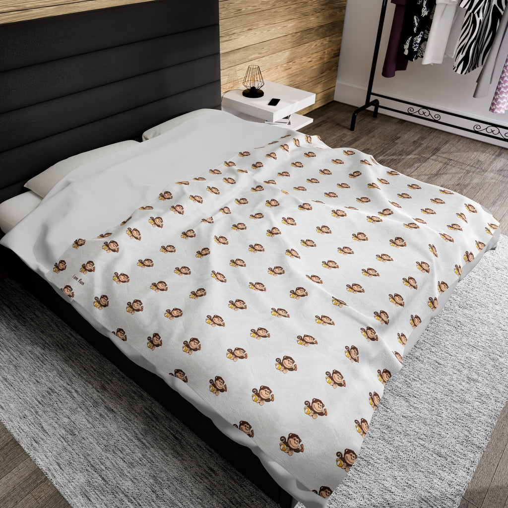 A 60 by 80 inch blanket on a queen-sized bed in a bedroom. The blanket has a repeating pattern of a monkey and the phrase “I am fun” in the bottom left corner.