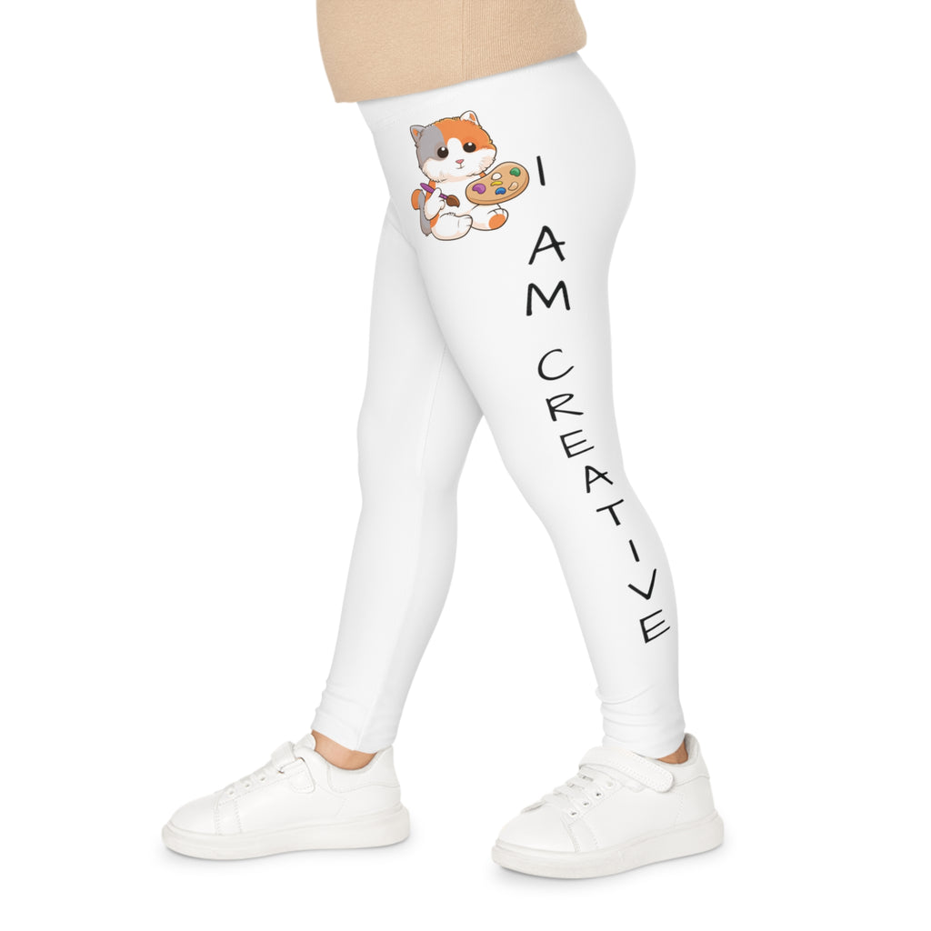 Left side-view of a child wearing white leggings with a picture of a cat on the front left waist and the phrase "I am creative" read top to bottom on the side of the leg.