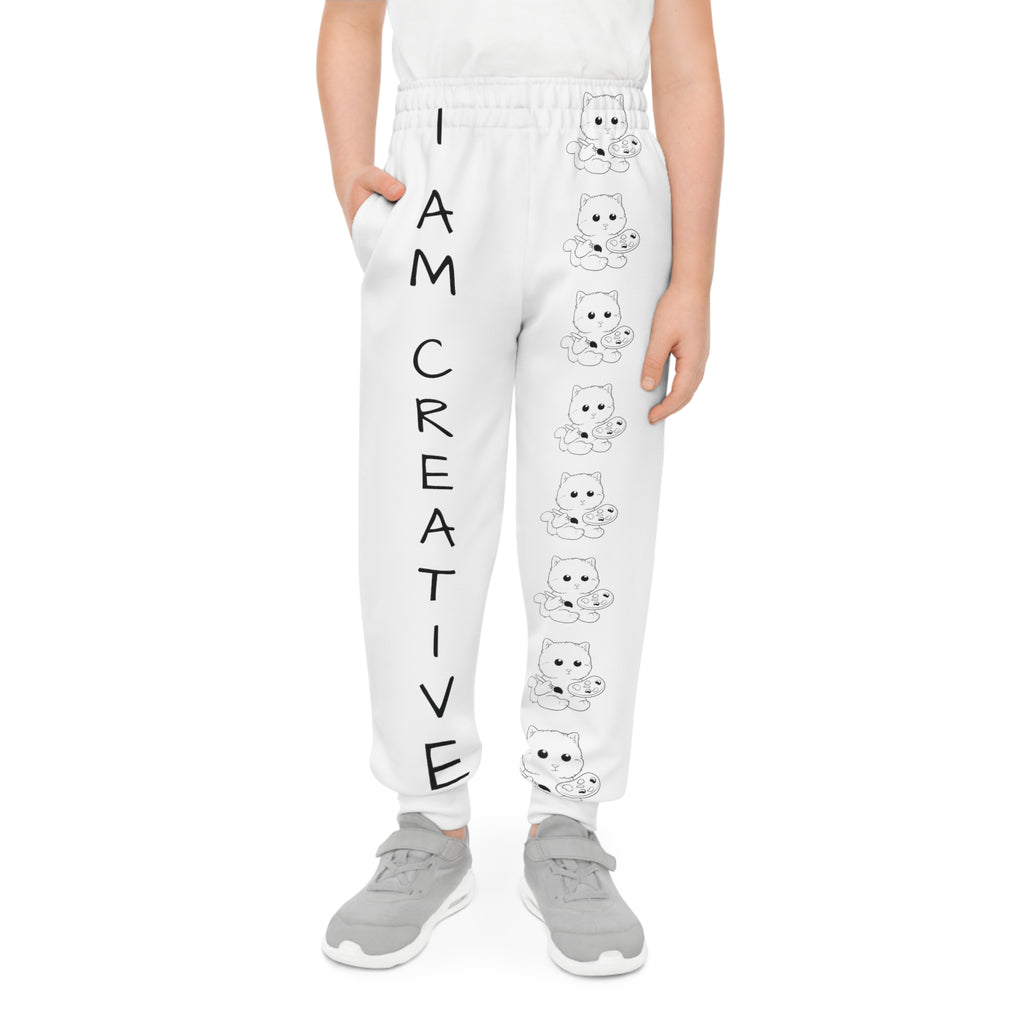 Front-view of a boy wearing white sweatpants with a line of black and white cats down the front left leg and the phrase "I am creative" down the front right leg.