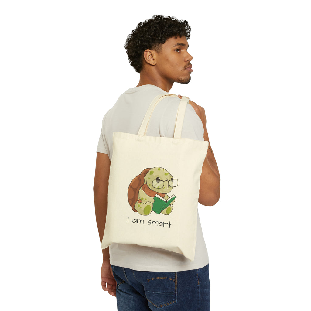 A man with a natural tan tote bag over his shoulder, featuring a picture of a turtle that says I am smart.
