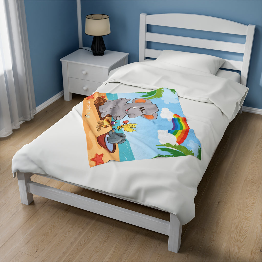 A 30 by 40 inch blanket on a twin-sized bed in a bedroom. The blanket has a scene of an elephant having a bonfire with a bird and fish on the beach, a rainbow in the background, and the phrase "I am calm" along the bottom.