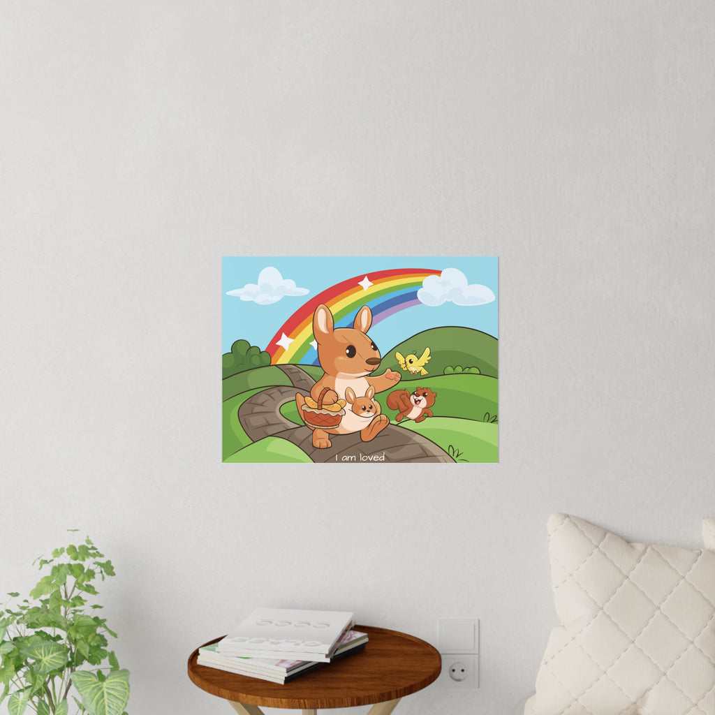 A 24 by 18 inch wall decal on a grey wall above a table and couch. The wall decal has a scene of a kangaroo walking along a path through rolling hills, a rainbow in the background, and the phrase "I am loved" along the bottom.