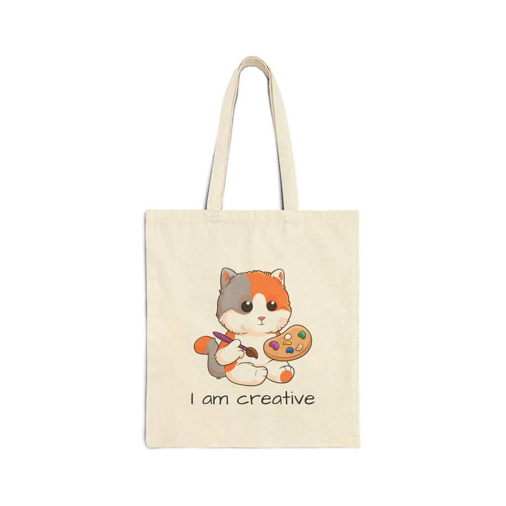 A natural tan tote bag with a picture of a cat that says I am creative.