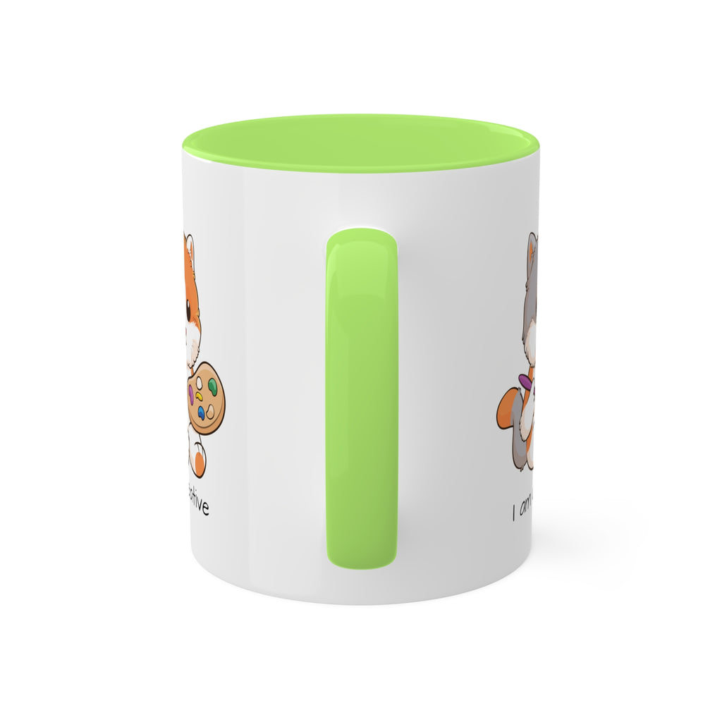 A white mug with a light green handle and interior and a picture of a cat that says I am creative.
