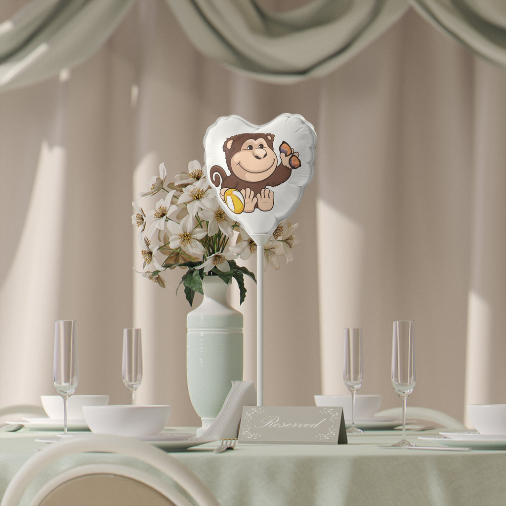A heart-shaped white mylar balloon on a stick with a picture of a monkey. The balloon sits on a table decorated for an event.