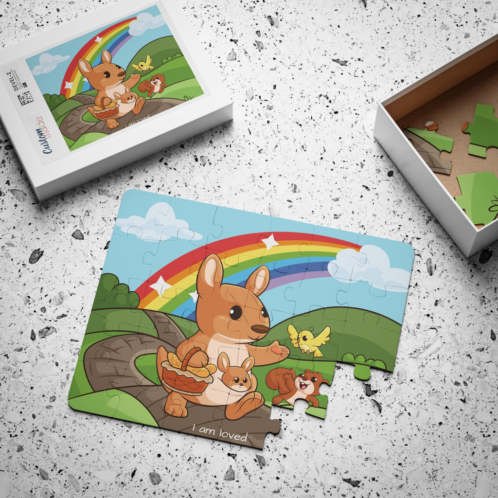 A 30 piece puzzle with a scene of a kangaroo walking on a path through rolling hills, a rainbow in the background, and the phrase "I am loved" along the bottom. The puzzle is mostly assembled next to its container box.