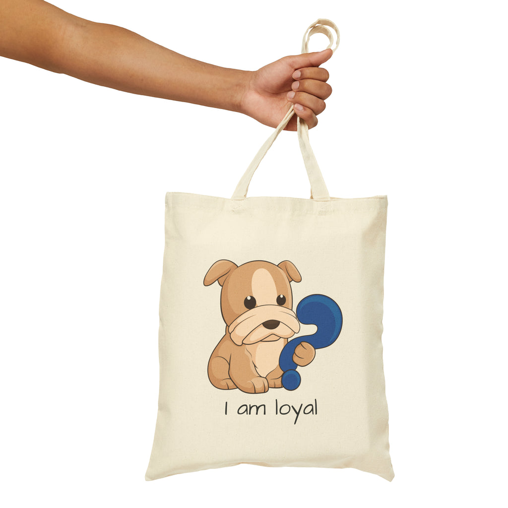A hand holding a natural tan tote bag with a picture of a dog that says I am loyal.