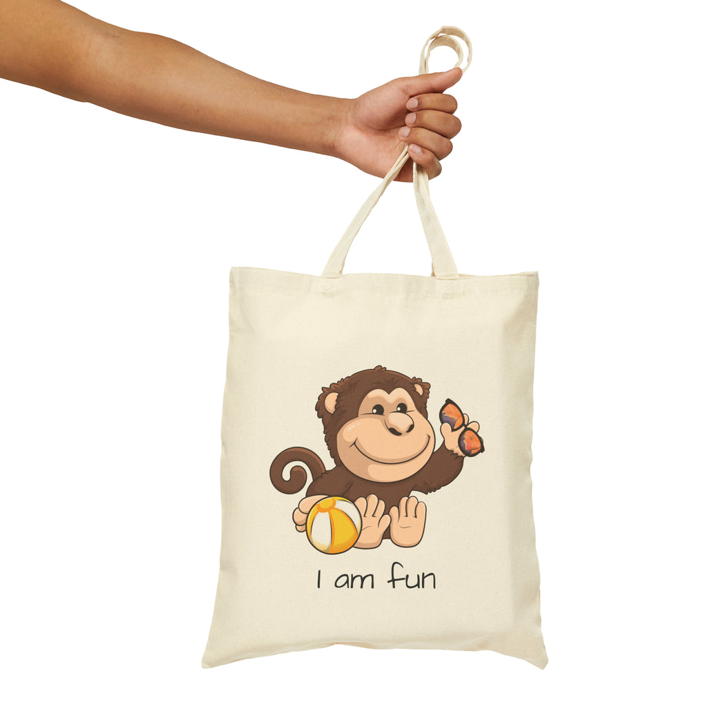 A hand holding a natural tan tote bag with a picture of a monkey that says I am fun.