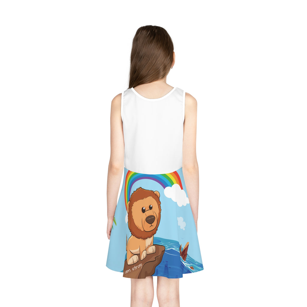 Back-view of a girl wearing a sleeveless dress. The dress has a white top and the skirt features a scene of a lion standing on a cliff over the ocean and the phrase "I am strong" along the bottom.