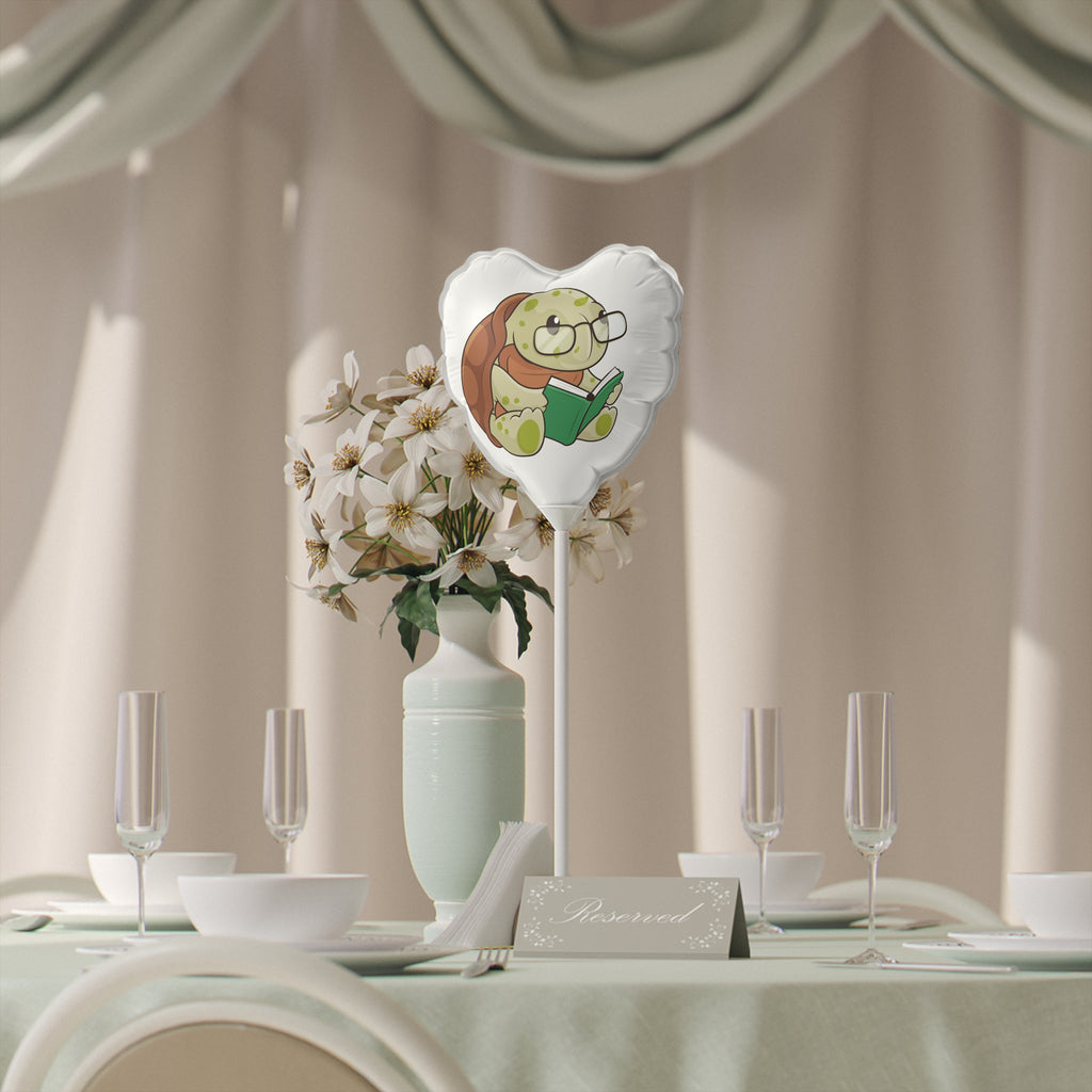 A heart-shaped white mylar balloon on a stick with a picture of a turtle. The balloon sits on a table decorated for an event.