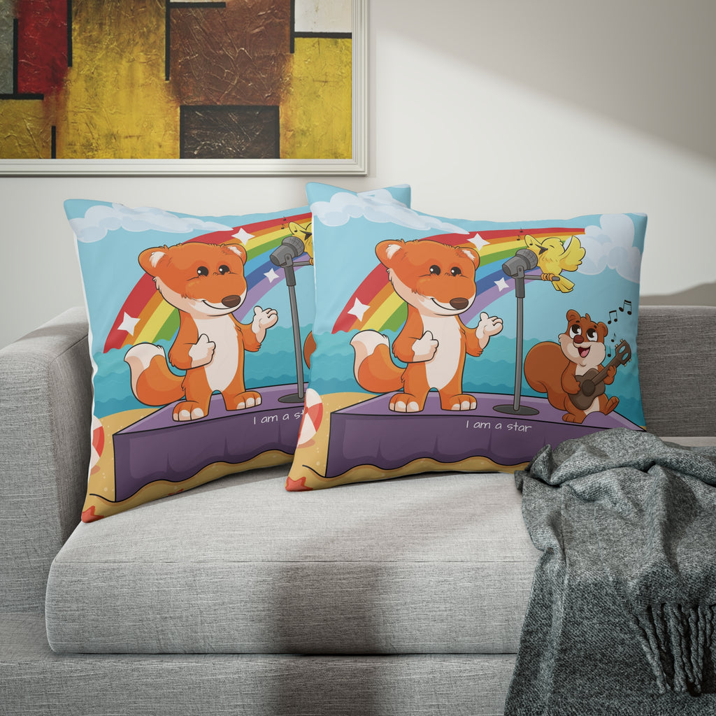 Two pillows sitting on a grey couch. The pillows have on pillowcases with a scene of a fox singing with a squirrel and bird on a stage on the beach, a rainbow in the background, and the phrase "I am a star" along the bottom.