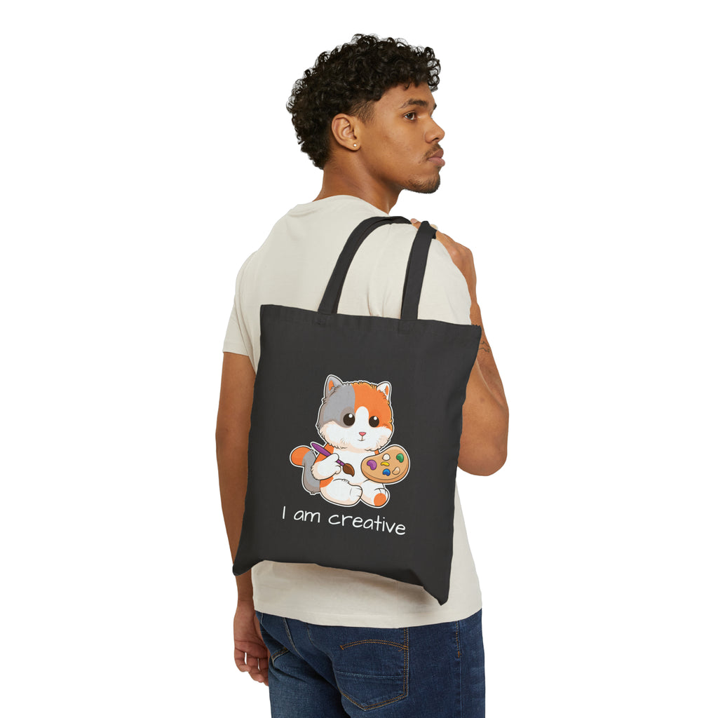 A man with a black tote bag over his shoulder, featuring a picture of a cat that says I am creative.