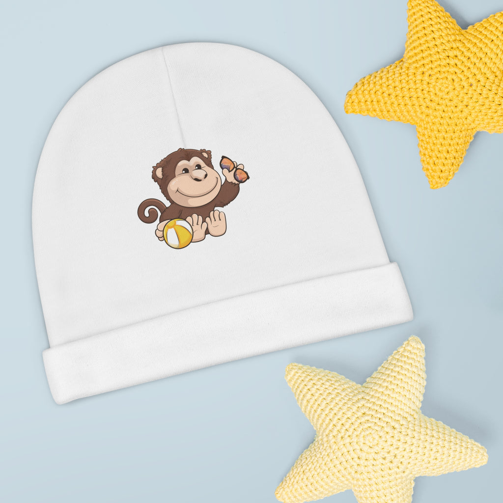 A white baby beanie with a small picture of a monkey. The beanie has the bottom edge folded up.
