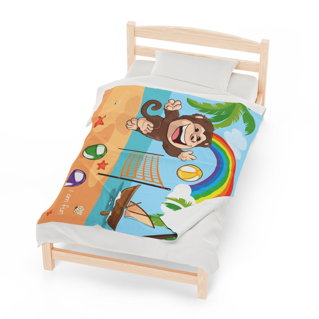 A 50 by 60 inch blanket on a twin-sized bed. The blanket has a scene of a monkey playing volleyball on the beach, a rainbow in the background, and the phrase "I am fun" along the bottom.