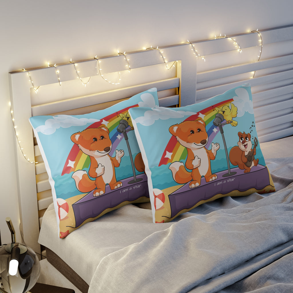Two pillows sitting on a bed. The pillows have on pillowcases with a scene of a fox singing with a squirrel and bird on a stage on the beach, a rainbow in the background, and the phrase "I am a star" along the bottom.
