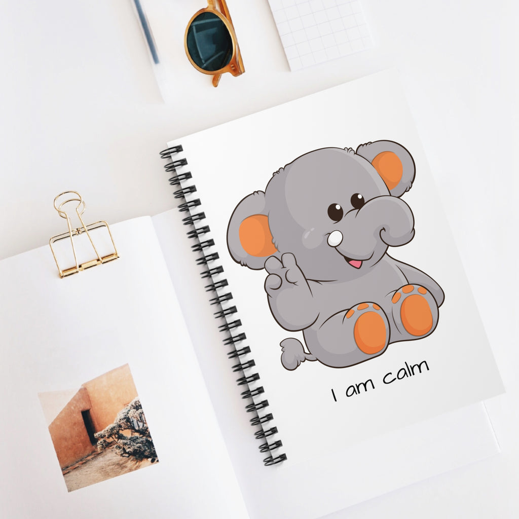 White spiral notebook with a picture of an elephant that says I am calm. The notebook is laying closed on a desk.