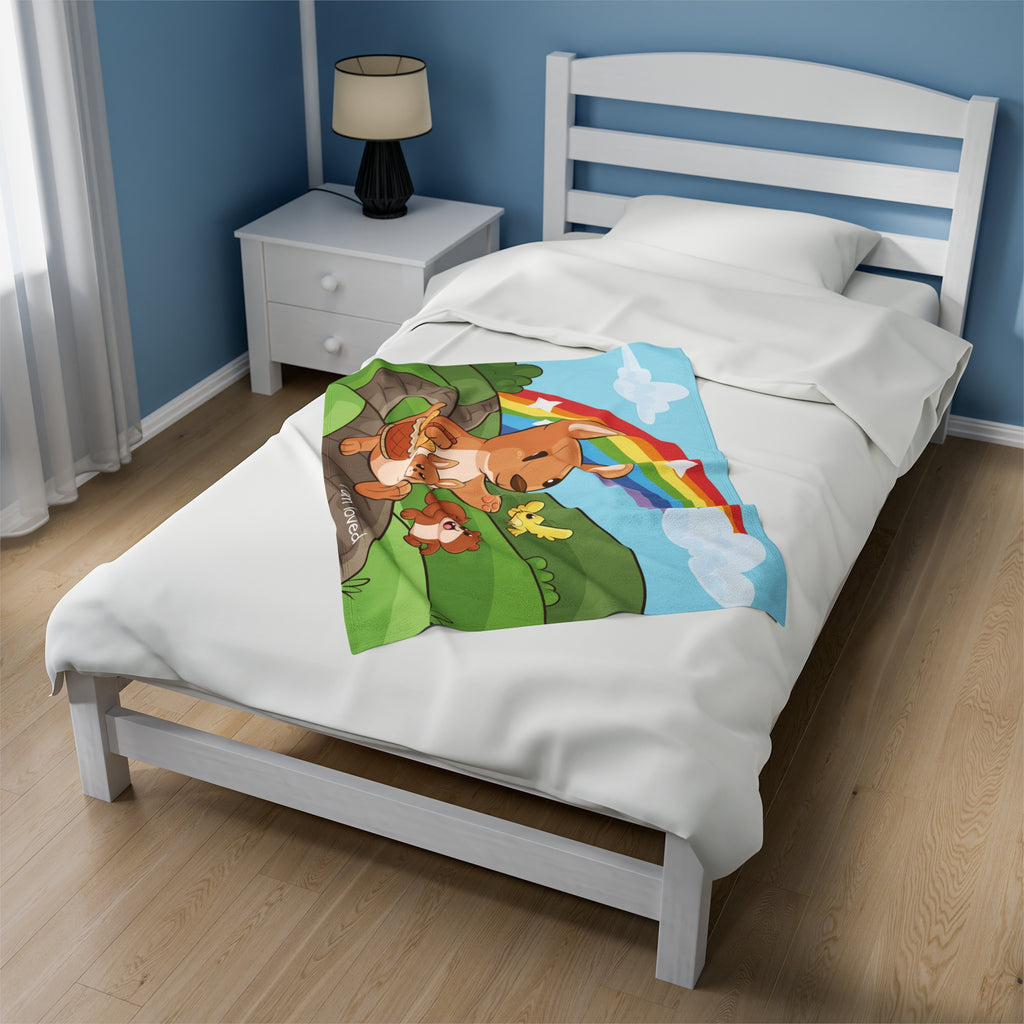 A 30 by 40 inch blanket on a twin-sized bed in a bedroom. The blanket has a scene of a kangaroo walking along a path through rolling hills, a rainbow in the background, and the phrase "I am loved" along the bottom.
