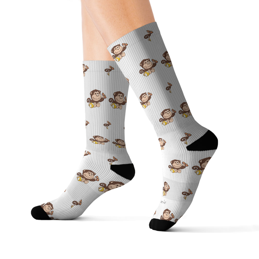 Feet wearing a pair of crew-length white socks with black toes and heels and a repeating pattern of a monkey.