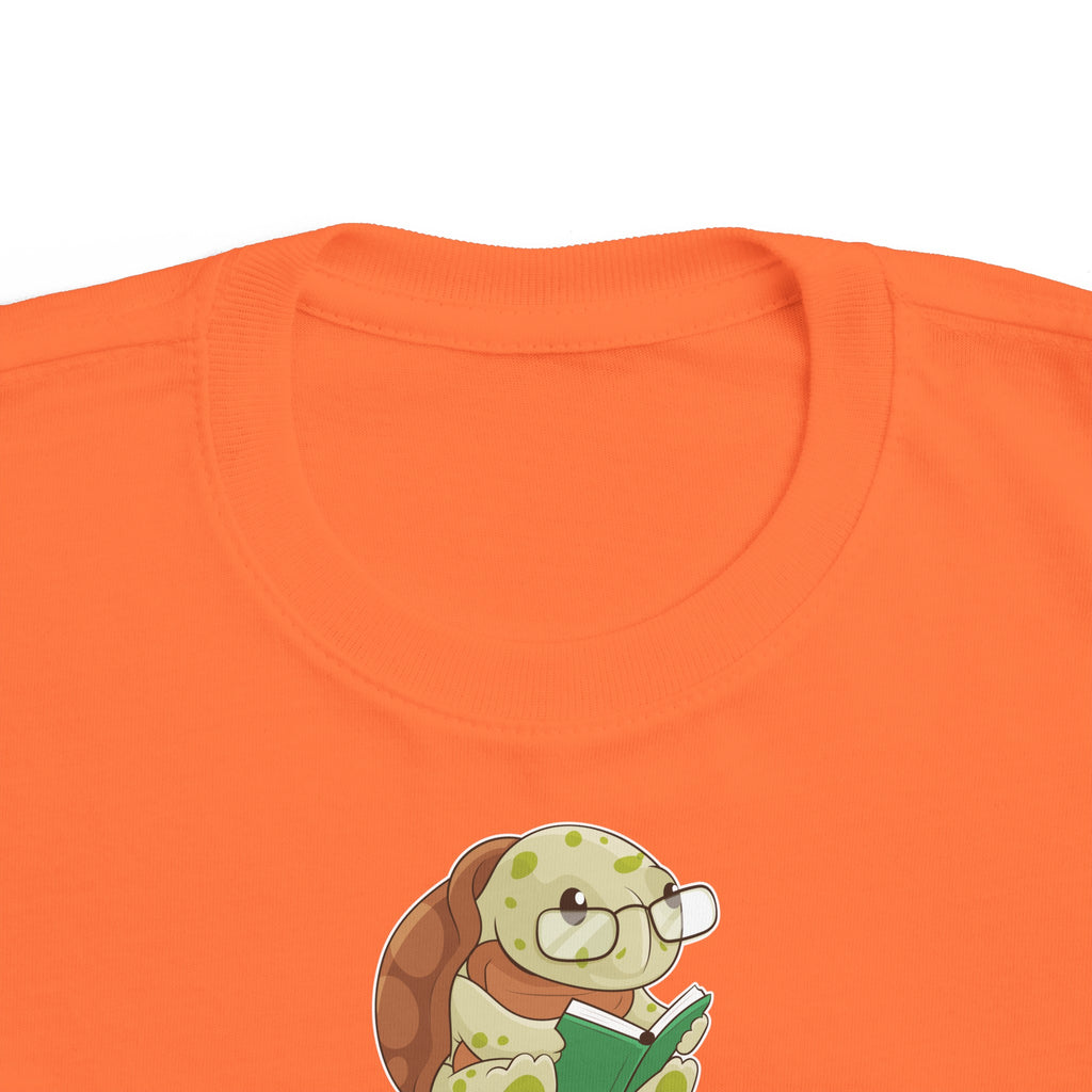 A close-up of the crew neckline of a short-sleeve orange shirt with a picture of a turtle that says Brainiac.