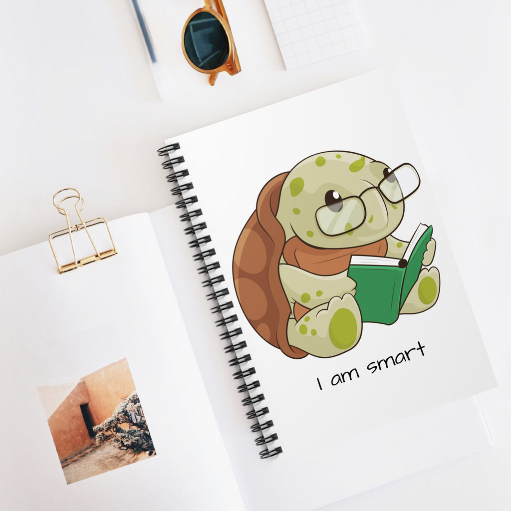 White spiral notebook with a picture of a turtle that says I am smart. The notebook is laying closed on a desk.