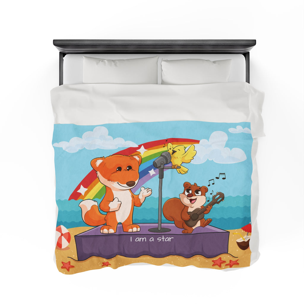 Top-view of a 60 by 80 inch blanket on a queen-sized bed. The blanket has a scene of a fox singing with a bird and squirrel on a stage on the beach, a rainbow in the background, and the phrase "I am a star" along the bottom.