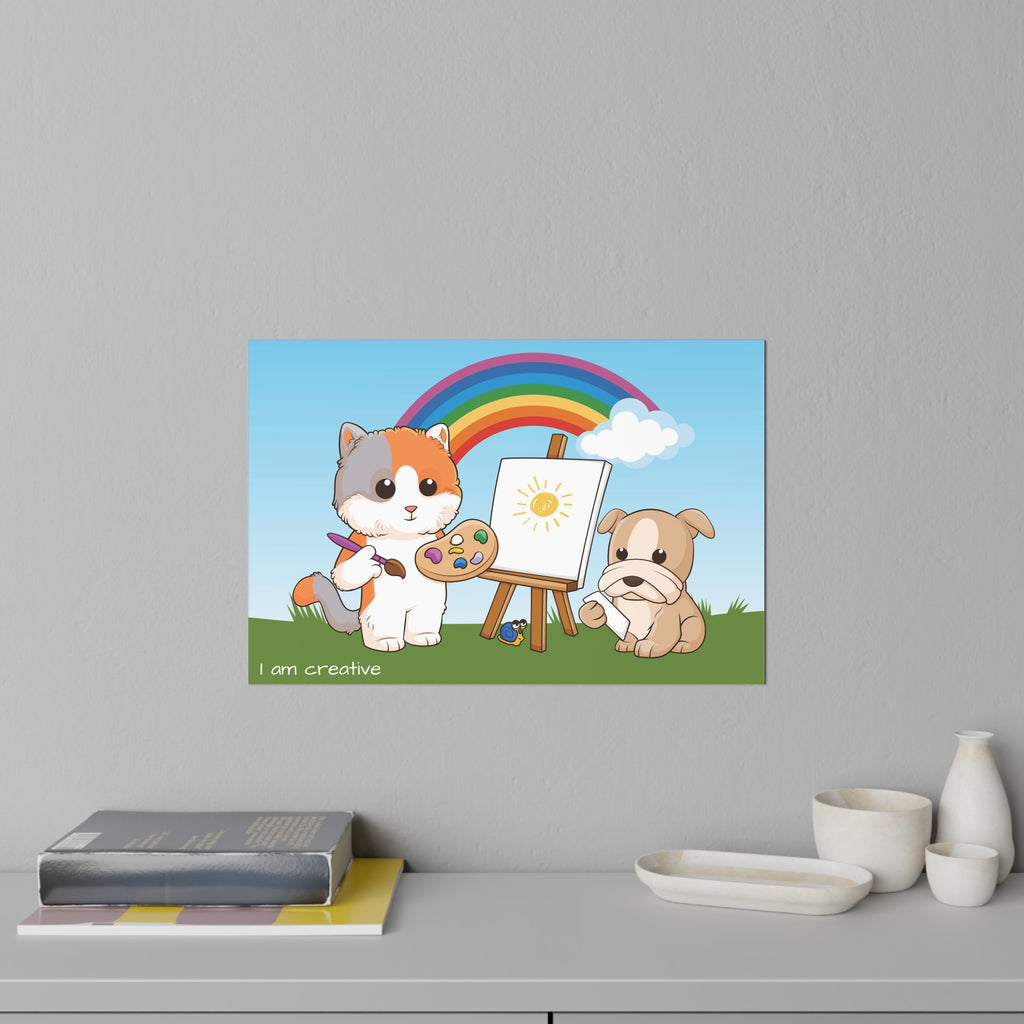 A 36 by 24 inch wall decal on a grey wall above a dresser and books. The wall decal has a scene of a cat painting on a canvas next to a dog, a rainbow in the background, and the phrase "I am creative" along the bottom.
