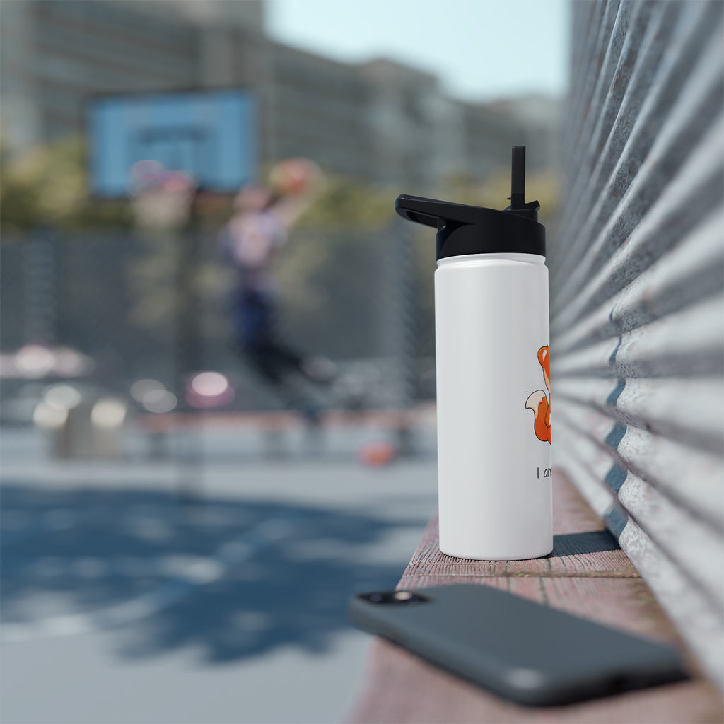 An 18 ounce white stainless steel water bottle with a black screw-on lid sitting on a basketball court bench. The bottle features a picture of a fox that says I am a star.