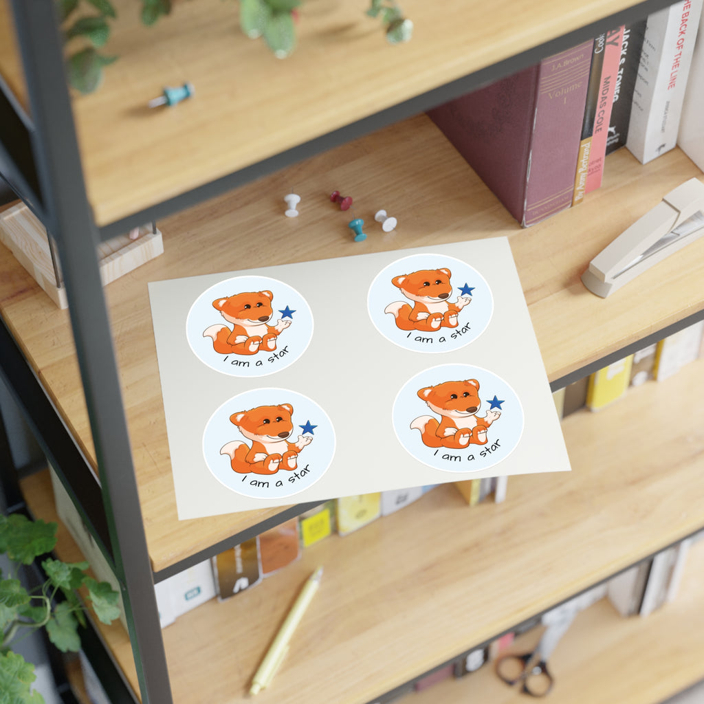A sheet of 4 round stickers with a picture of a fox that says I am a star. The sticker sheet sits on a shelf of a bookcase.
