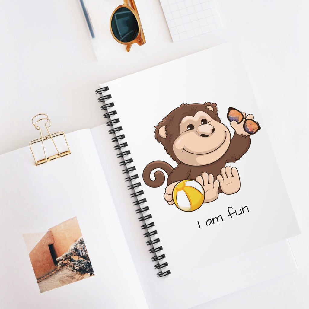 White spiral notebook with a picture of a monkey that says I am fun. The notebook is laying closed on a desk.
