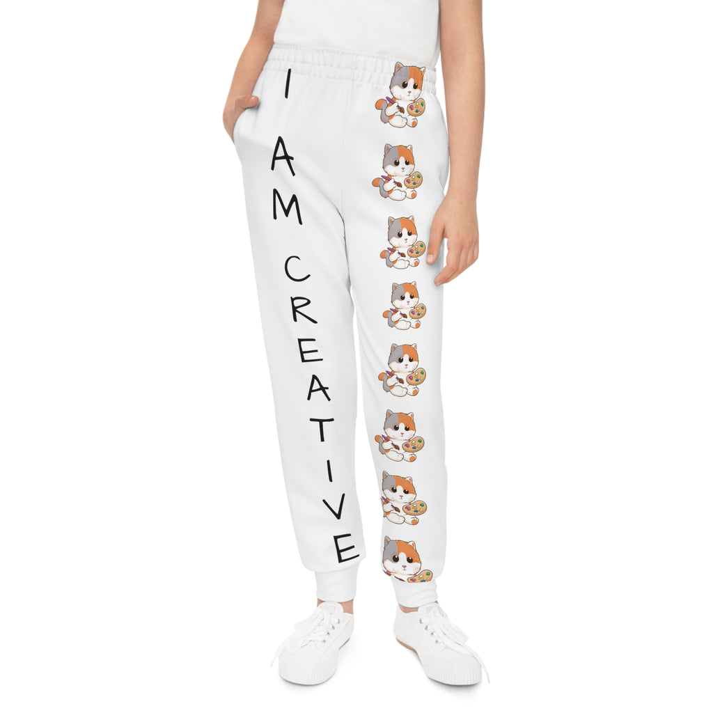 Front-view of a girl wearing white sweatpants with a line of cats down the front left leg and the phrase "I am creative" down the front right leg.