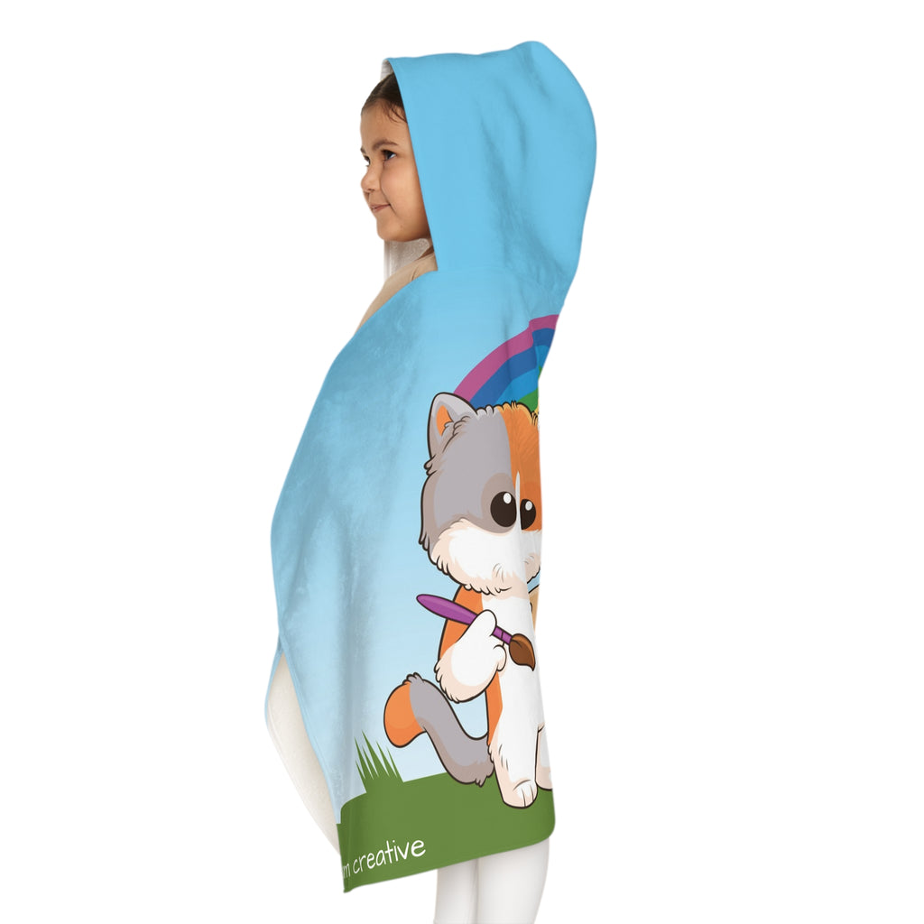 Left side-view of a girl wearing a hooded towel and holding it closed around her. The towel has a scene of a cat painting on a canvas next to a dog, a rainbow in the background, and the phrase "I am creative" along the bottom.