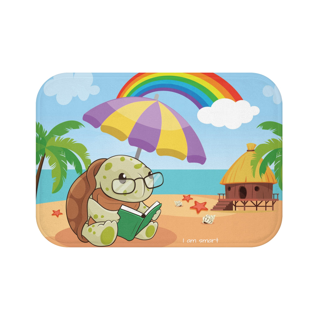 A 24 by 17 inch bath mat that has a scene of a turtle reading under an umbrella on a beach with a rainbow in the background and the phrase "I am smart" along the bottom.